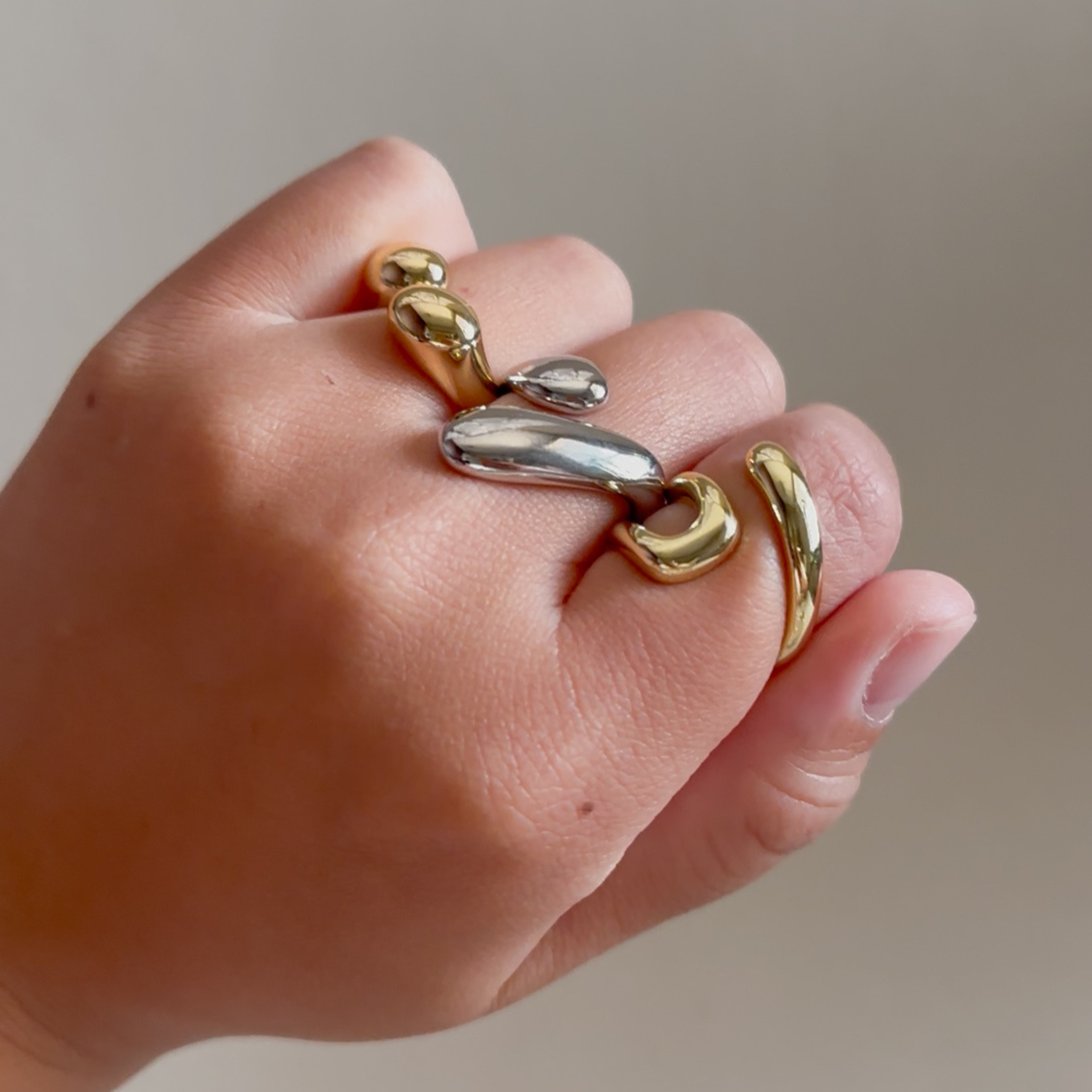 Hand wearing multiple gold and silver rings on a neutral background